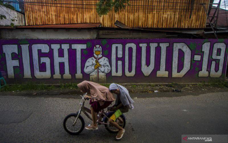 Dua anak mengayuh sepeda di dekat mural kampanye penanggulangan COVID-19 di Banjarmasin, Kalimantan Selatan, Senin (17/5/2021). (foto : ANTARA FOTO/BAYU PRATAMA S)