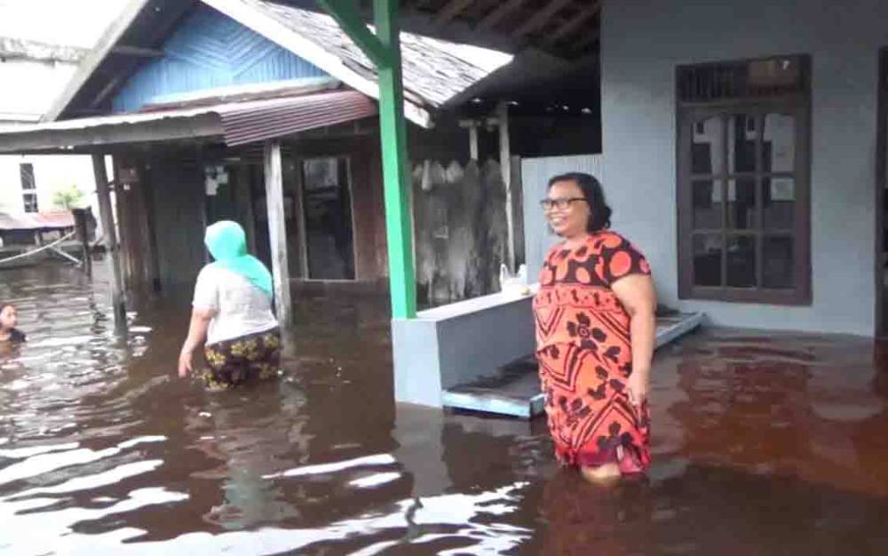 Sejumlah warga berada di depan rumahnya di tengah banjir yang melanda.