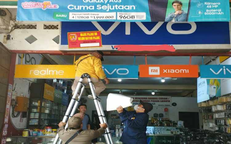 Saat petugas Bapenda dan Satpol PP Kobar memasang stiker di toko yang tak taat wajib pajak. (FOTO : BAPENDA KOBAR)