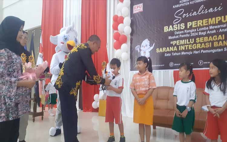 Ketua KPU Kobar, Chaidir menyerahkan piala dan boneka maskot kepada salah satu anak yang telah memenangkan lomba mewarnai dalam acara Sosialisasi Basis Perempuan yang termasuk rangkaian kegiatan kirab pemilu 2024, Jumat, 19 Mei 2023 (FOTO: NURITA)