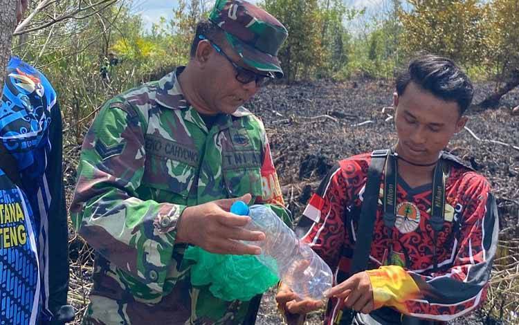 Babinsa Kelurahan Kereng Bangkirai Sertu Eko Cahyono saat memegang barang bukti botol plastik berisi sisa BBM. (FOTO: IST)