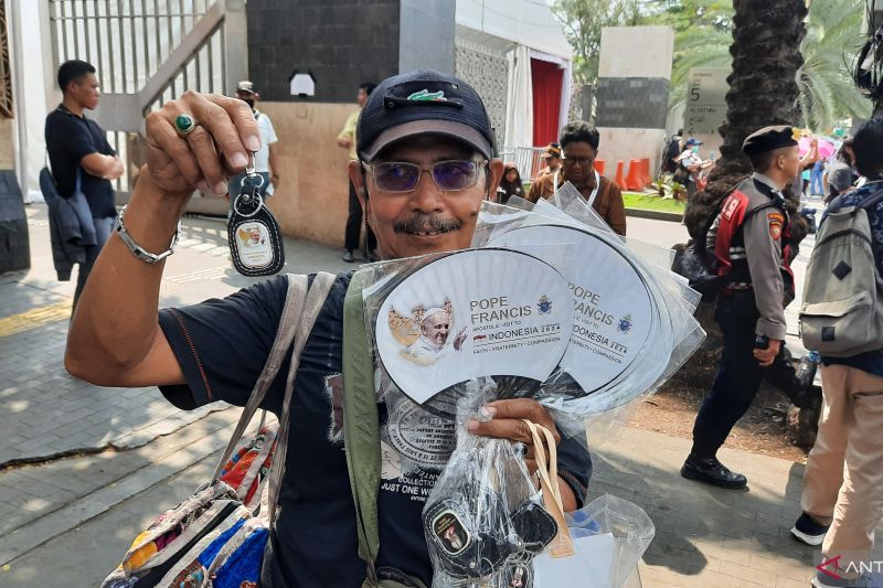 Seorang pedagang menunjukkan kipas dan gantungan kunci dengan gambar Pemimpin umat Katolik dunia sekaligus Kepala Negara Vatikan Paus Fransiskus di seberang Gereja Katedral Jakarta, Rabu (4/9/2024). (ANTARA/Lia Wanadriani Santosa)