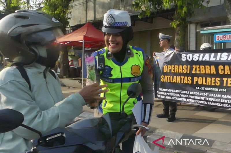 Seorang Polwan memberikan setangkai bunga kepada pengandara yang tertib berlalu lintas. ANTARA/Heru Suyitno