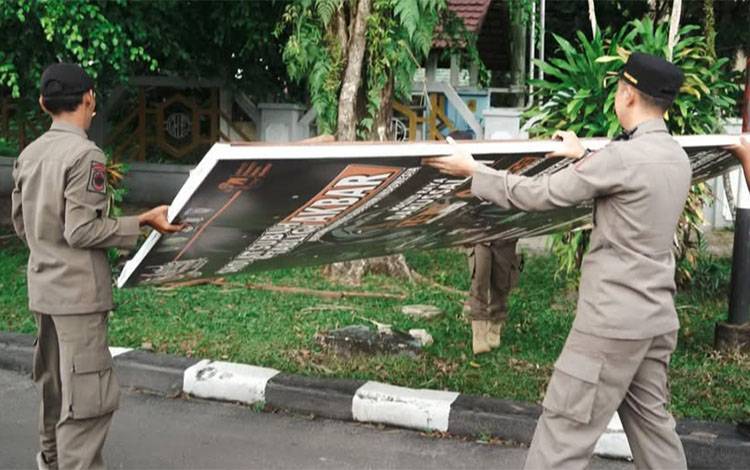 Petugas menurunkan reklame tak berizin di Palangka Raya. (FOTO: HUMAS)