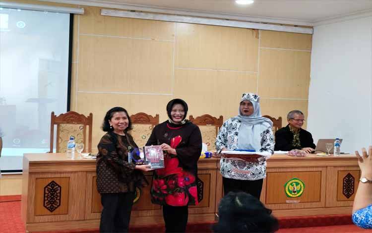 Ketua Umum HISKI, Novi Anoegrajekti (tengah) didampingi Ketua HISKI Komisariat Kalimantan Tengah, Alifiah Nurachmana (kanan) menyerahkan buku dan plakat kepadb? Wakil Rektor Universitas Palangka Raya, Natalina Asi.(FOTO: TESTI PRISCILLA)