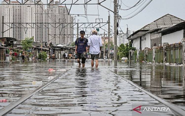 Warga melintasi perlintasan kereta yang terendam banjir di kawasan Kampung Bandan, Jakarta, Minggu (18/1/2026). Genangan air dampak curah hujan tinggi merendam perlintasan kereta di kawasan Kampung Bandan sehingga perjalanan KRL Cikarang Line hanya bisa dilayani sampai Stasiun Kemayoran dan Angke, serta KRL Bogor Line hanya bisa dilayani sampai Stasiun Jayakarta dan Manggarai. ANTARA FOTO/Sulthony Hasanuddin/nym.